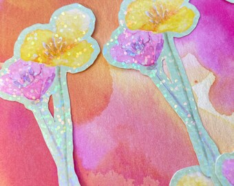 May include: Close-up of floral stickers featuring yellow and pink watercolour flowers. The stickers have a pale blue outline with iridescent glitter. The background is an orange and pink watercolour wash.