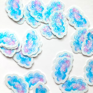 May include: Cloud-shaped stickers with a watercolour design in shades of blue and purple, with glitter accents. Each sticker has a white border and a glossy finish. Ideal for scrapbooking or crafts.