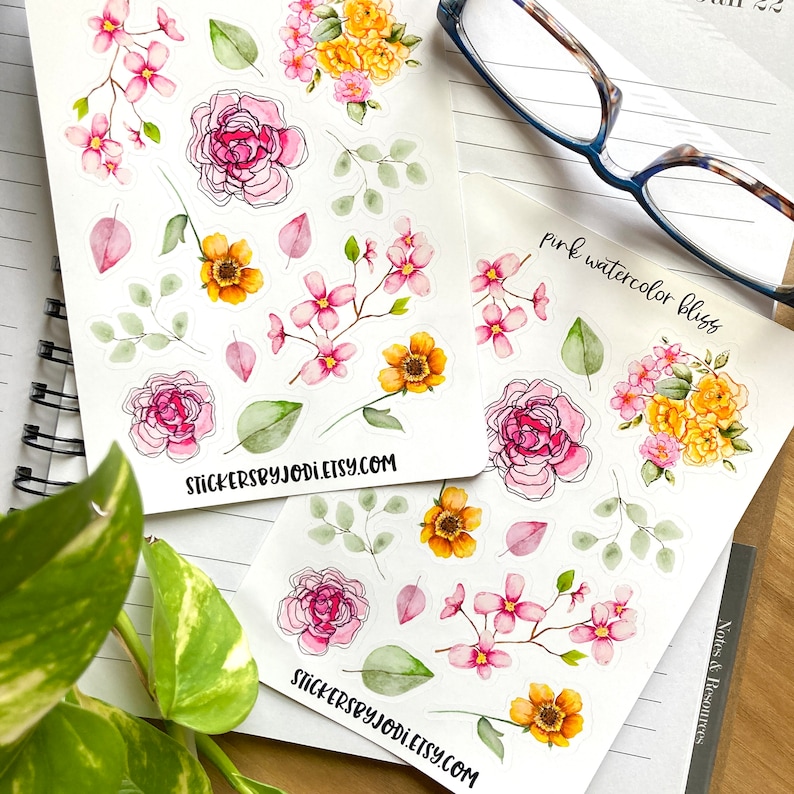 May include: Two sticker sheets featuring watercolor floral designs. The stickers include pink roses, yellow and pink blossoms, and green leaves. One sheet has the text "pink watercolor bliss". The website address stickersbyjodi.etsy.com is printed on the bottom of each sheet.