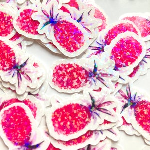 Puede incluir: Un conjunto de pegatinas con forma de piña. Cada pegatina presenta un diseño de piña roja y brillante con un contorno blanco y detalles verdes y morados. Las pegatinas están dispersas sobre una superficie blanca.