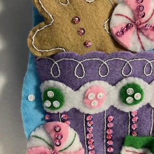 May include: A handmade felt Christmas stocking with a gingerbread man, candy, and other festive decorations. The stocking is primarily blue, purple, and white, with pink and green accents. Embellished with sequins and buttons.