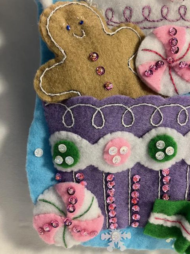 May include: A handmade felt Christmas stocking with a gingerbread man, candy, and other festive decorations. The stocking is primarily blue, purple, and white, with pink and green accents. Embellished with sequins and buttons.