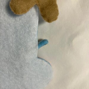 May include: Close-up of a light blue felt snowman with a brown felt antler. The snowman has a small blue felt arm. The felt is soft and textured.