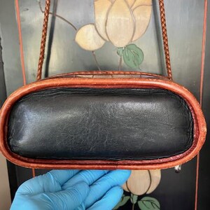 May include: A black leather crossbody bag with a brown leather trim. The bag has a braided strap and a flap closure.