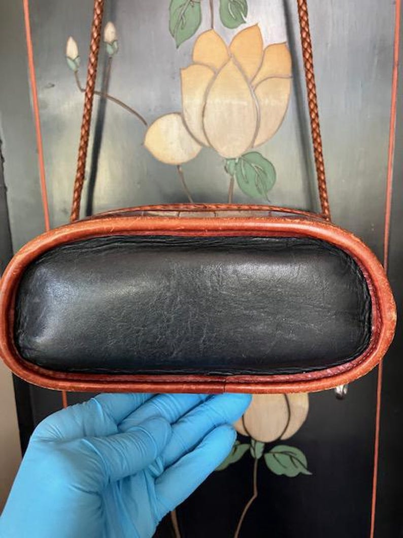 May include: A black leather crossbody bag with a brown leather trim. The bag has a braided strap and a flap closure.