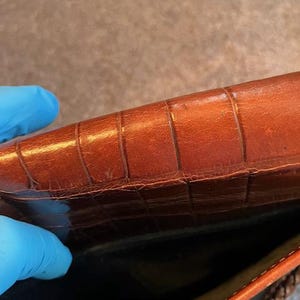 May include: The inside of a brown leather handbag with a woven strap. The leather has a crocodile-embossed pattern.