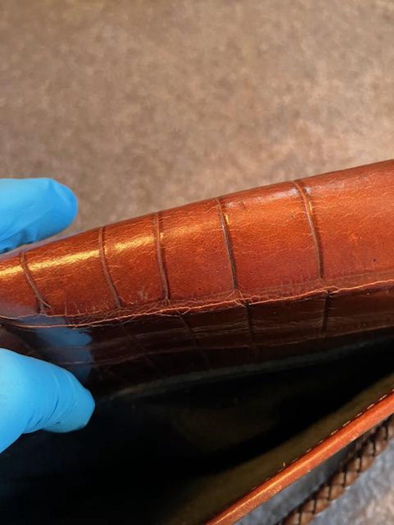 May include: The inside of a brown leather handbag with a woven strap. The leather has a crocodile-embossed pattern.