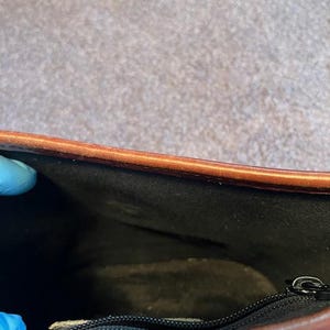 May include: Inside view of a brown leather bag with a black fabric lining and a zipper closure.