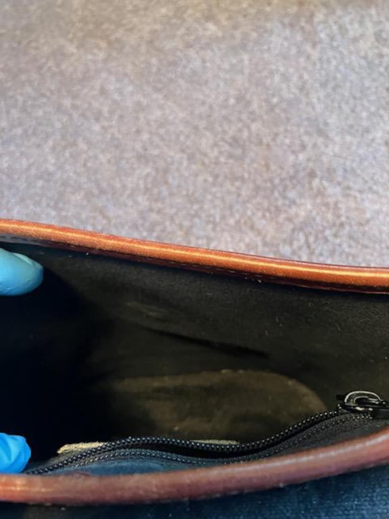 May include: Inside view of a brown leather bag with a black fabric lining and a zipper closure.