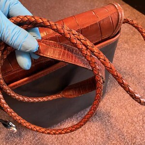 May include: A brown leather handbag with a braided strap. The bag has a crocodile-embossed design.