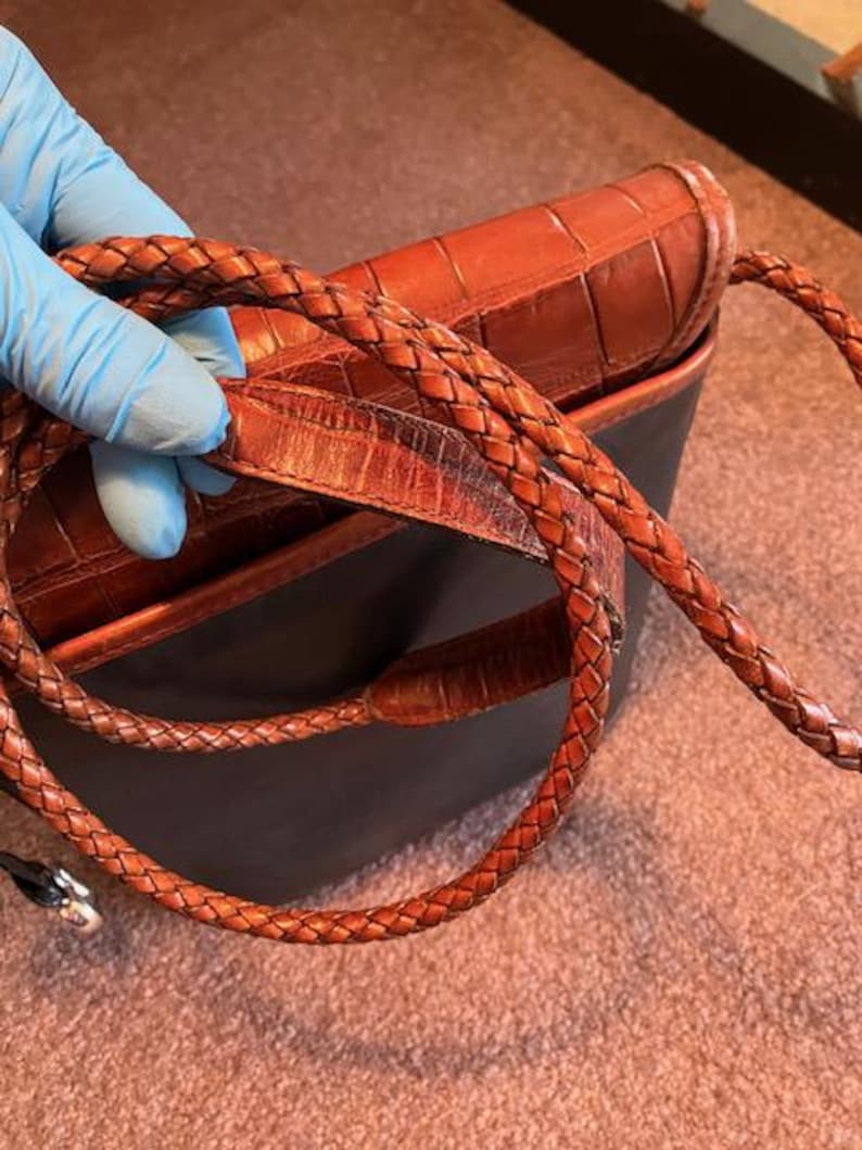 May include: A brown leather handbag with a braided strap. The bag has a crocodile-embossed design.