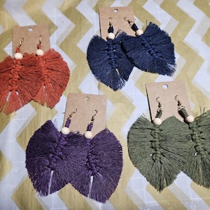 Puede incluir: Cuatro pares de pendientes de borla hechos a mano con cuentas de madera. Los pendientes son en tonos de morado, azul, verde y naranja.