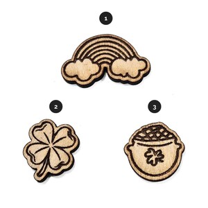 May include: Three wooden St. Patrick's Day themed embellishments: a rainbow, a four-leaf clover, and a pot of gold. Each piece is made of light-colored wood with a dark outline, perfect for crafts and decorations.