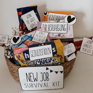 Könnte beinhalten: Ein geflochtener Korb voller Snacks und Leckereien, darunter Süßigkeiten und Kaugummi. Der Korb hat mehrere kleine Schilder mit deutschem Text, darunter "New Job Survival Kit". Das Gesamtthema ist ein Geschenkkorb.