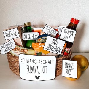 Könnte beinhalten: Ein geflochtener Korb gefüllt mit verschiedenen Artikeln, darunter Flaschen und Päckchen, beschriftet mit deutschen Texten. Der Korb ist mit "SCHWANGERSCHAFT SURVIVAL KIT" mit einem Herzsymbol beschriftet. Zwei Zitronen liegen neben dem Korb.