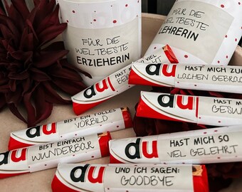 May include: A collection of small red and white chocolate bars with the word "du" printed on them. Each bar has a different message, including "For the best teacher", "You are a great role model", and "You have taught me so much".
