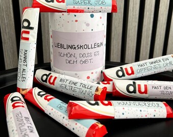 Puede incluir: Una colección de barras de chocolate envueltas en papel de colores con diferentes mensajes escritos en ellas. Los mensajes incluyen "Haces un gran trabajo", "Eres un gran jugador de equipo", "Eres un gran representante", "Siempre tienes un oído atento", "Eres maravilloso", y "Puedes hacer todo".