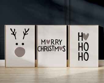 Puede incluir: Tres impresiones enmarcadas con fondo blanco y texto negro. La impresión de la izquierda presenta una cara de reno de dibujos animados con cuernos marrones y una nariz marrón. La impresión del medio dice "Merry Christmas" con un pequeño corazón que reemplaza la "o" de "Merry" y la "s" de "Christmas". La impresión de la derecha dice "Ho Ho Ho" con un corazón marrón que reemplaza la "o" del primer "Ho".