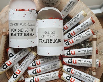 May include: A collection of chocolate bars wrapped in white paper with red polka dots and personalized messages in German. The messages include "Du bist die tollste Schwester", "Danke für alles", "Für die beste Brautjungfer", "Für die welbeste Trauzeugin", "Du bist einfach wunderbar", "Hast neben mir gestromt", "Du bist einfach die beste", "Du bist die tollste Organisatorin", "Du hast den besten JBA organisiert", "Du hattest so viele tolle Ideen", "Du warst uns so eine grosse Hilfe", "Du hast ein Danke verdient", "Du hattest super Nerven", "Du hast so viel zum Detour gebracht", "Du hattest immer ein offenes Ohr", "Du warst immer für uns da".