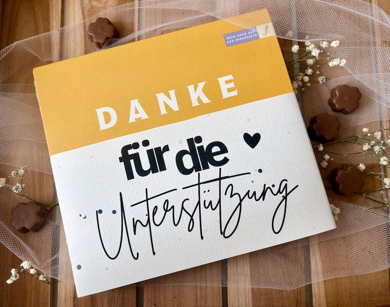 May include: A rectangular card with a yellow top section and a white bottom section. The word "DANKE" is printed in white block letters on the yellow section. The words "f&uuml;r die Unterst&uuml;tzung" are printed in black script on the white section.