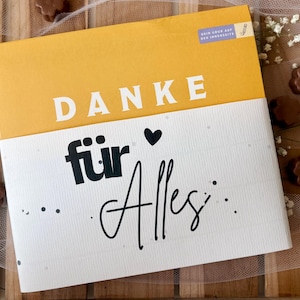 May include: A greeting card with the words "DANKE f&uuml;r Alles" in white and black lettering. The top portion of the card is yellow, and the bottom is white. The card is decorated with a small black heart and dots.