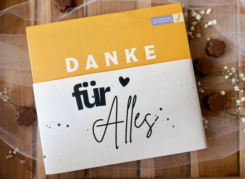 May include: A greeting card with the words "DANKE f&uuml;r Alles" in white and black lettering. The top portion of the card is yellow, and the bottom is white. The card is decorated with a small black heart and dots.