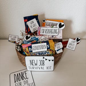 Puede incluir: Una cesta de mimbre llena de aperitivos y golosinas, incluyendo caramelos y productos envasados. La cesta incluye varios letreros peque&ntilde;os con texto como "New Job Survival Kit" y "Gracias". El tema general es una cesta de regalo.