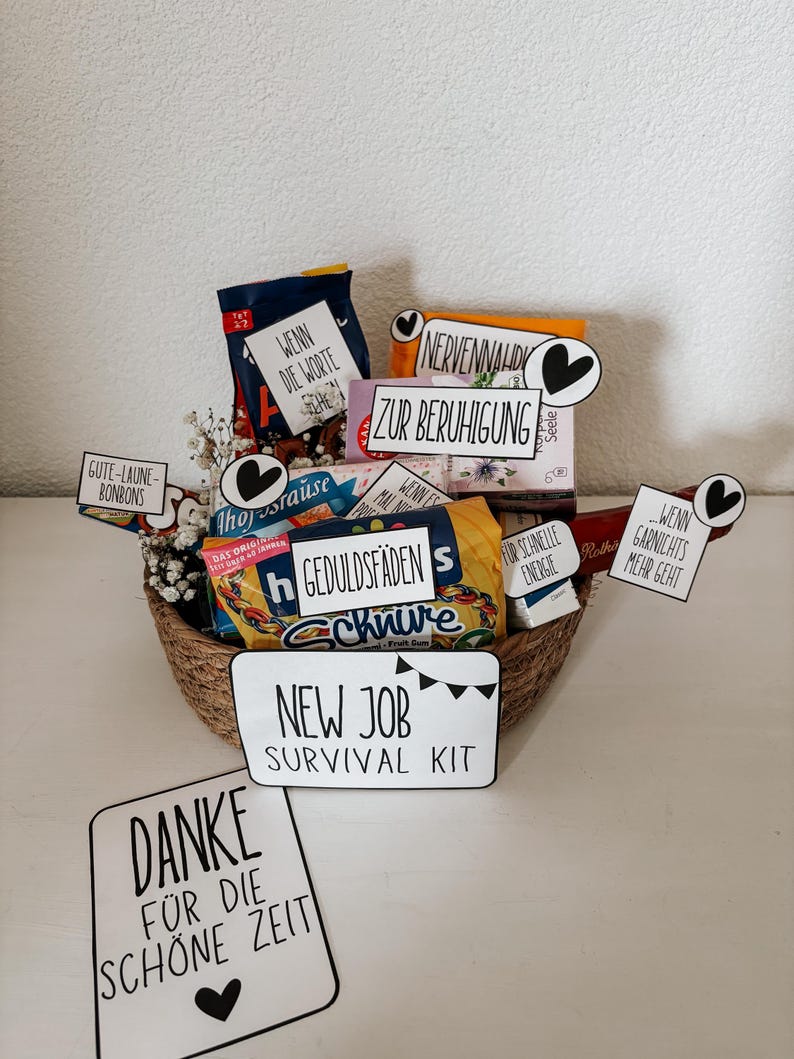 Puede incluir: Una cesta de mimbre llena de aperitivos y golosinas, incluyendo caramelos y productos envasados. La cesta incluye varios letreros peque&ntilde;os con texto como "New Job Survival Kit" y "Gracias". El tema general es una cesta de regalo.