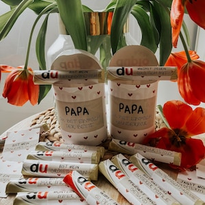 May include: A collection of small wrapped chocolate bars with various messages printed on them. The messages include "Du bist mein lieblingsmensch", "Du bist einfach der beste", "Du bist einfach wunderbar", "Geburtstag", "F&uuml;r alles, f&uuml;r uns", "Du bist mein gr&ouml;&szlig;ter Fan", "F&uuml;r mich", "Munter, immer", "Gibst immer 100 Prozent", "Bist einfach wunderbar", "Du bist das beste unserer Familie", "Pflegs mich gesund", "Jagst morgen weiter", "Gutes Nacht-Kasse", "Ein Joker".