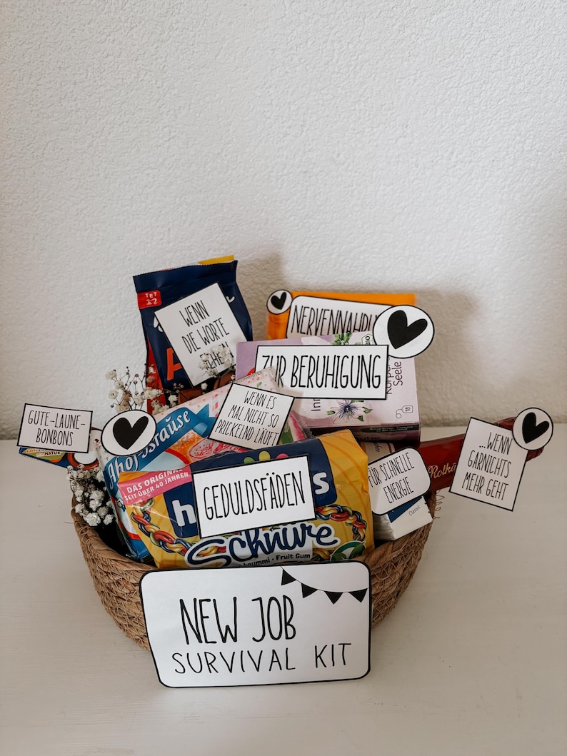 Puede incluir: Una cesta de mimbre llena de snacks y golosinas, incluyendo caramelos y chicles. La cesta tiene varios letreros peque&ntilde;os con texto en alem&aacute;n, incluyendo "New Job Survival Kit". El tema general es una cesta de regalo.