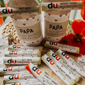 May include: A collection of small wrapped chocolate bars with the word "du" printed on them. Each bar has a different message printed on the wrapper, such as "You are my biggest fan" and "You are simply wonderful".