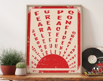 May include: A red and white poster with the words "CONFIDENT CREATIVE STRONG SUNSHINE" written in a circular pattern. The poster is framed in a light wood frame and is hanging on a white wall above a wooden table.