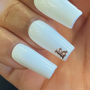 May include: White long, square-shaped acrylic nails with a gold accent on one nail. The accent is a small, ornate design.