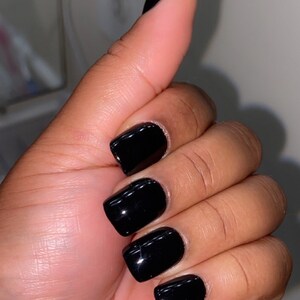 May include: Close-up of a hand with short, square-shaped nails painted black.