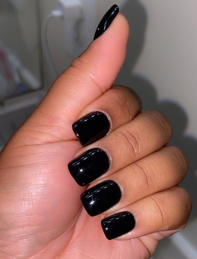 May include: Close-up of a hand with short, square-shaped nails painted black.