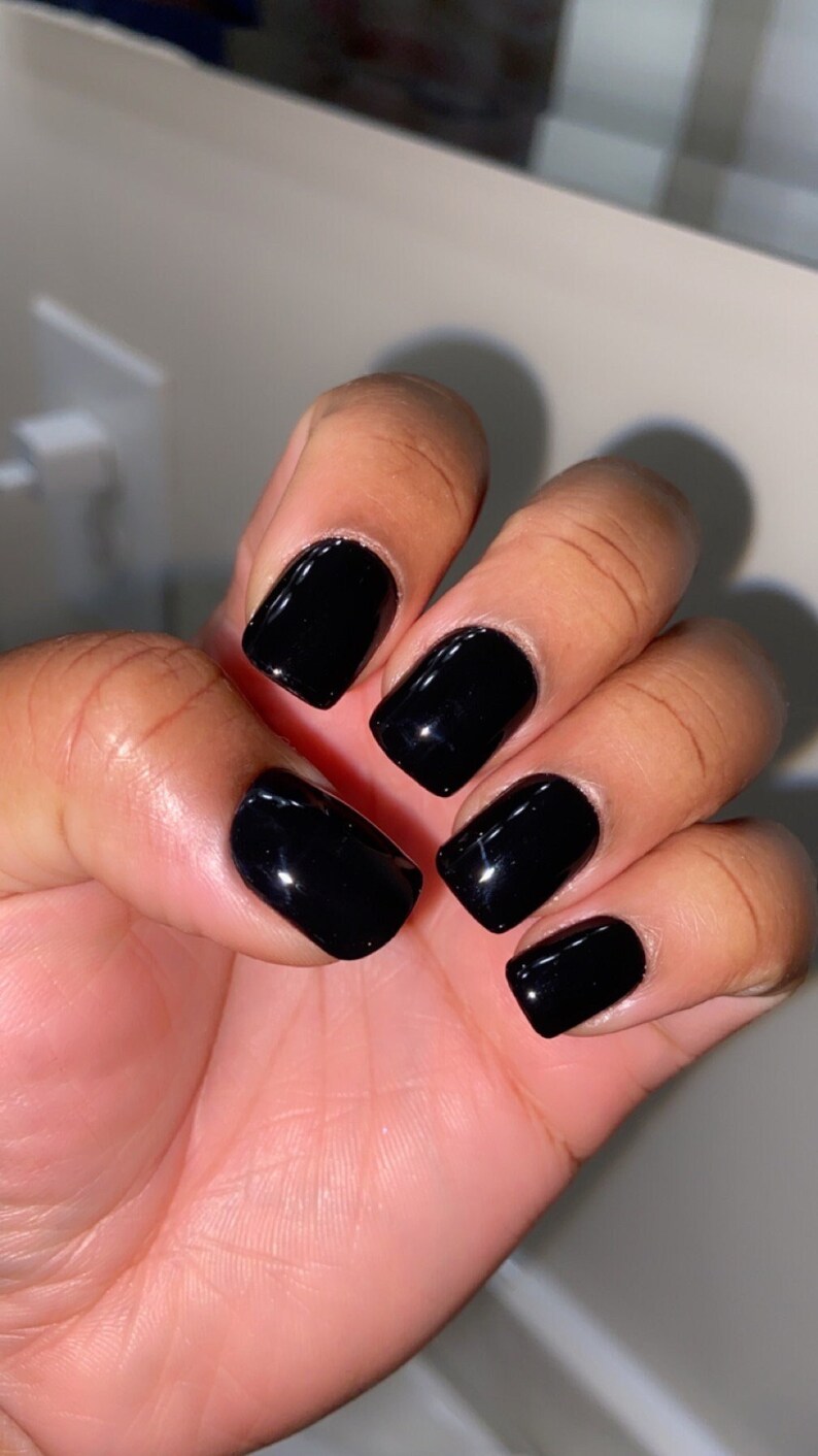 May include: Close-up of a hand with short, square-shaped nails painted black.