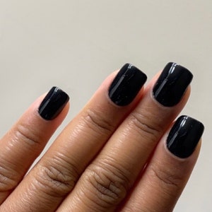 May include: Close-up of a hand with four black square-shaped nails painted with a glossy black nail polish.