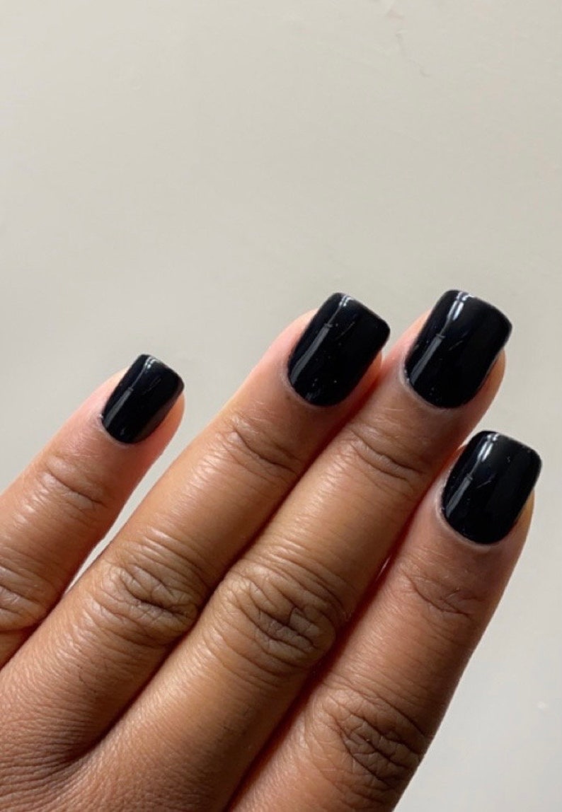 May include: Close-up of a hand with four black square-shaped nails painted with a glossy black nail polish.