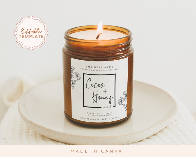 May include: A brown glass candle jar with a white label. The label has a black border and features the text "BUSINESS NAME", "ORGANIC | VEGAN | CRUELTY FREE", "Cocoa + Honey", "Soy Candles", "NET WT 8 OZ / 226 G", "40 HOUR BURN TIME", and "HANDPOURED IN AUSTIN, TEXAS".