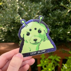 May include: A green alien puppy sticker with three eyes and a galaxy background. The sticker says "ZEEP GLORP" at the bottom.