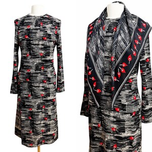 Peut inclure: Une robe vintage à manches longues avec une écharpe assortie. La robe présente un motif noir, blanc et gris avec des touches de rouge. L'écharpe est noire avec une bordure blanche et des motifs floraux rouges. La robe est de longueur midi.