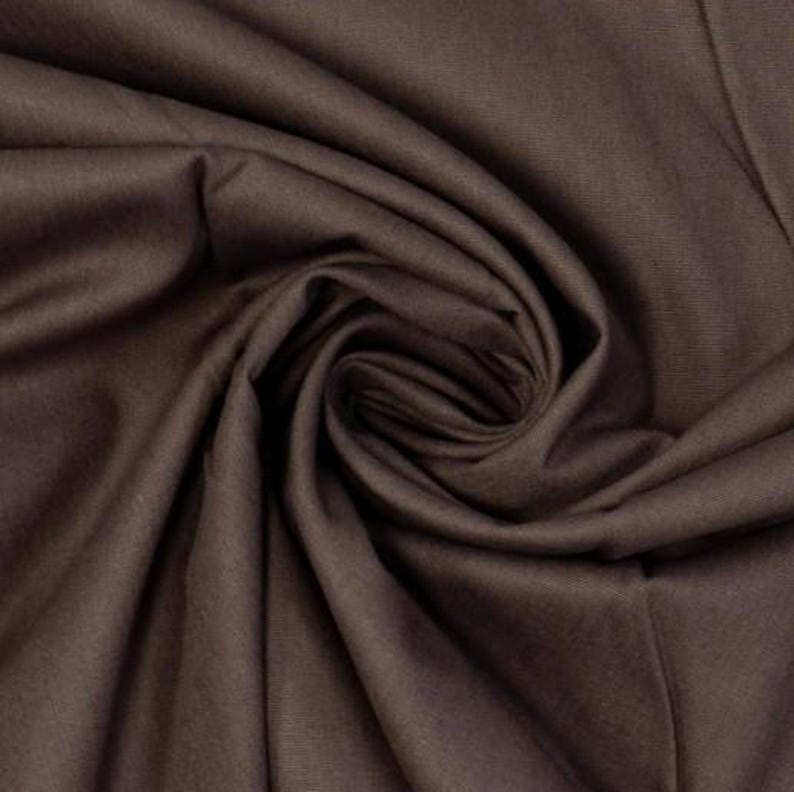 May include: A solid dark brown fabric with a smooth, matte texture. The material is gathered in the center, creating deep, flowing folds and shadows that highlight the consistent, uniform color and the soft, pliable nature of the textile.