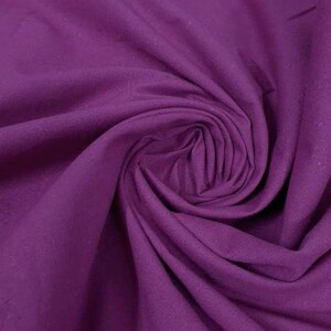 May include: A solid deep purple fabric with a smooth, matte texture. The material is gathered into a central spiral swirl, creating soft, flowing folds and shadows that highlight the consistent, rich violet color across the entire surface.