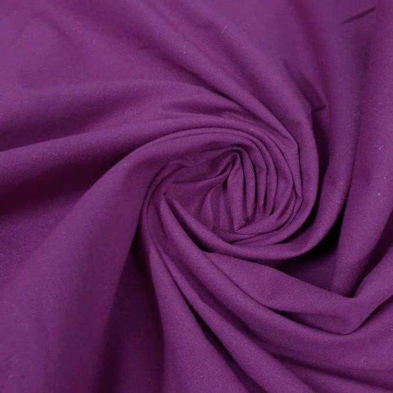 May include: A solid deep purple fabric with a smooth, matte texture. The material is gathered into a central spiral swirl, creating soft, flowing folds and shadows that highlight the consistent, rich violet color across the entire surface.