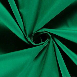 May include: A solid emerald green fabric with a smooth, matte texture. The material is gathered in the center, creating deep, radiating folds and shadows that highlight the vibrant, saturated green color and the consistent weave of the textile.