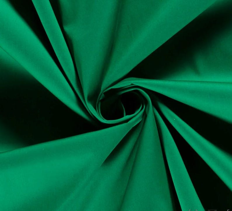 May include: A solid emerald green fabric with a smooth, matte texture. The material is gathered in the center, creating deep, radiating folds and shadows that highlight the vibrant, saturated green color and the consistent weave of the textile.