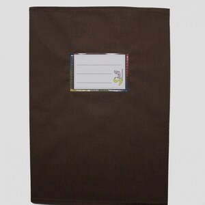 May include: A rectangular dark brown fabric pouch featuring a central white label window with three horizontal lines for writing. The label is bordered by a thin, multicolored rainbow-patterned trim and includes the green text logo toffi.