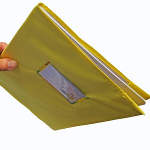 May include: A bright yellow fabric binder cover featuring a clear rectangular plastic window on the front panel. The cover is designed to hold a notebook or document folder, with visible white paper pages inside the yellow textile casing.