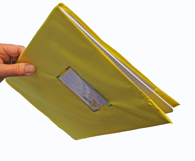 May include: A bright yellow fabric binder cover featuring a clear rectangular plastic window on the front panel. The cover is designed to hold a notebook or document folder, with visible white paper pages inside the yellow textile casing.