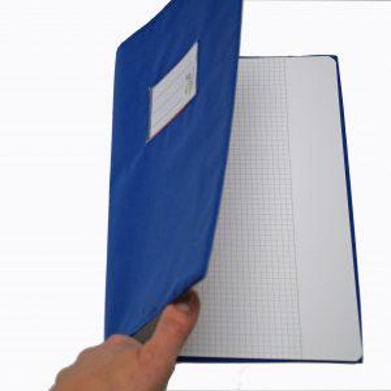 May include: A blue notebook with a flexible cover featuring a clear plastic label holder on the front. The notebook is partially open, revealing white pages with a grid pattern printed in light gray lines throughout the interior paper sheets.
